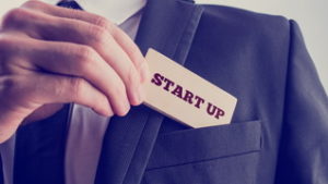 Businessman removing a wooden card reading Start up from the pocket of his suit jacket, vintage effect toned image.